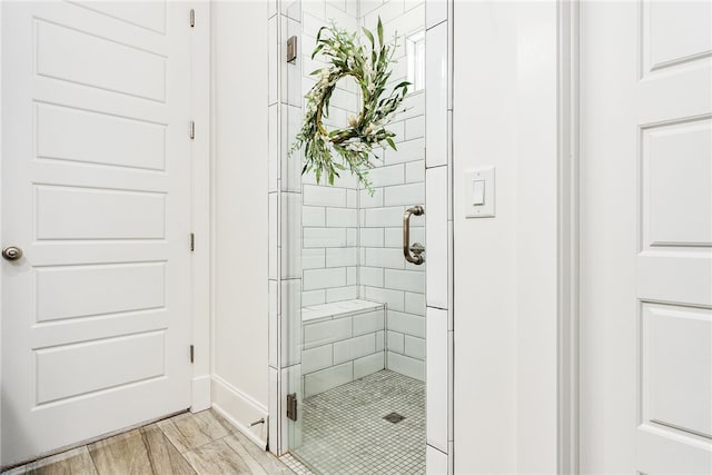 full bath featuring wood finished floors, a stall shower, and baseboards