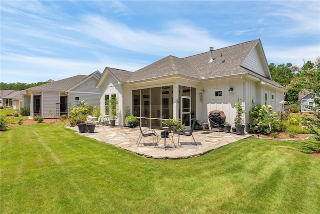 rear view of house featuring a patio, a lawn, board and batten siding, and a sunroom