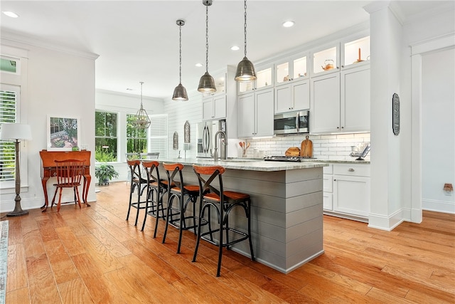 kitchen with stainless steel microwave, ornamental molding, light wood-type flooring, and decorative backsplash