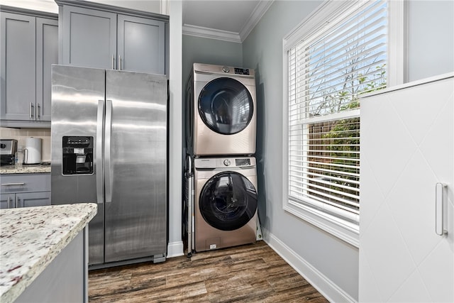 clothes washing area with crown molding, baseboards, laundry area, stacked washer and clothes dryer, and dark wood-style flooring