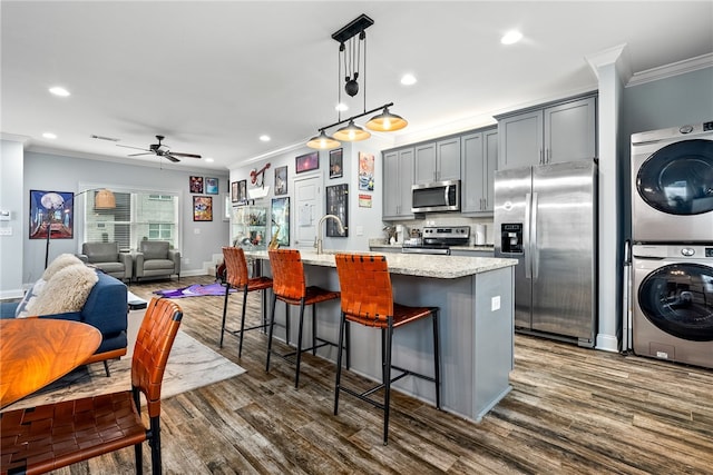 kitchen featuring a center island with sink, a breakfast bar, dark wood-style flooring, stainless steel appliances, and stacked washer and dryer