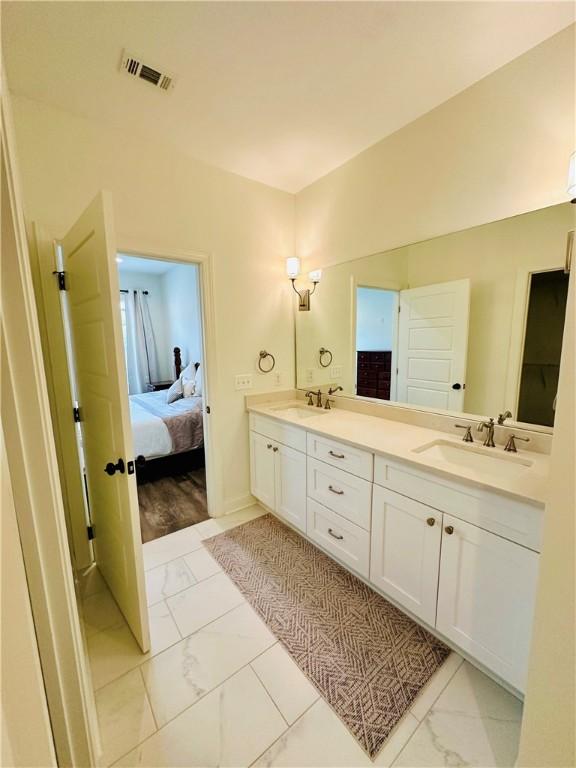 bathroom with double vanity, connected bathroom, a sink, visible vents, and marble finish floor