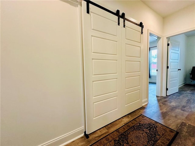 hallway featuring dark wood-type flooring, a barn door, and baseboards