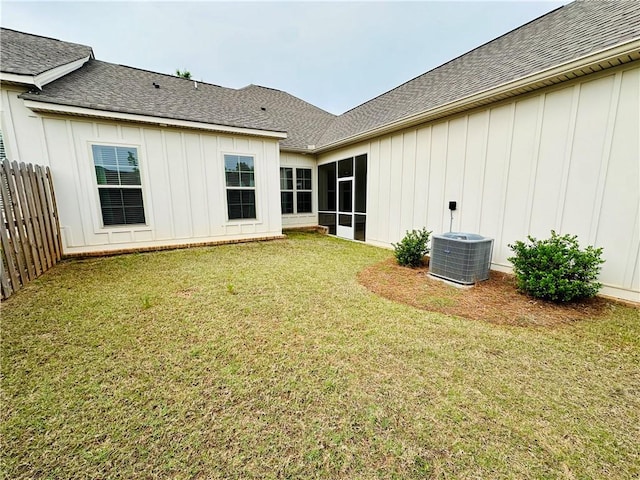 back of property with cooling unit, fence, a lawn, board and batten siding, and roof with shingles