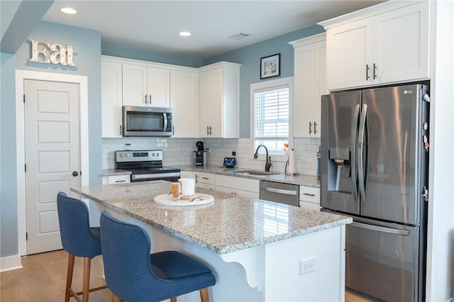 kitchen featuring a center island, white cabinets, sink, light stone countertops, and stainless steel appliances