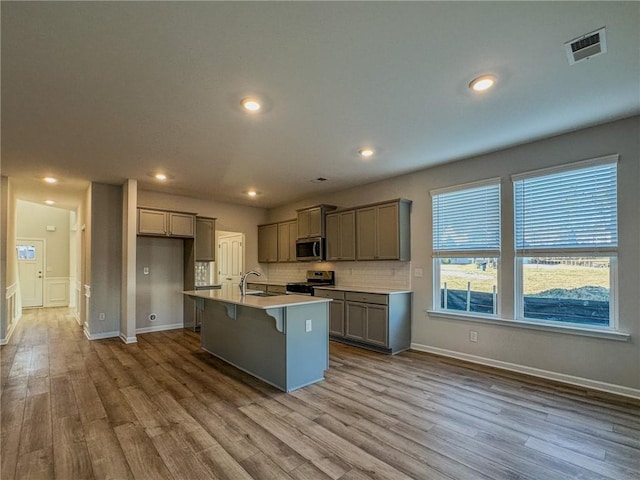 kitchen with light hardwood / wood-style floors, a breakfast bar area, stainless steel appliances, a kitchen island with sink, and sink