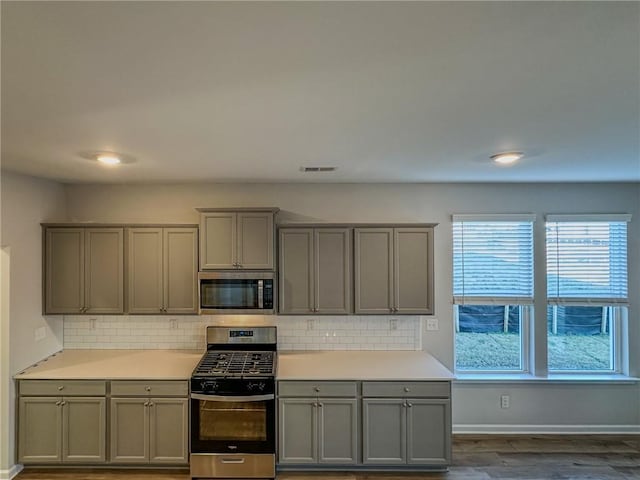 kitchen with dark wood-type flooring, stainless steel appliances, gray cabinetry, and backsplash