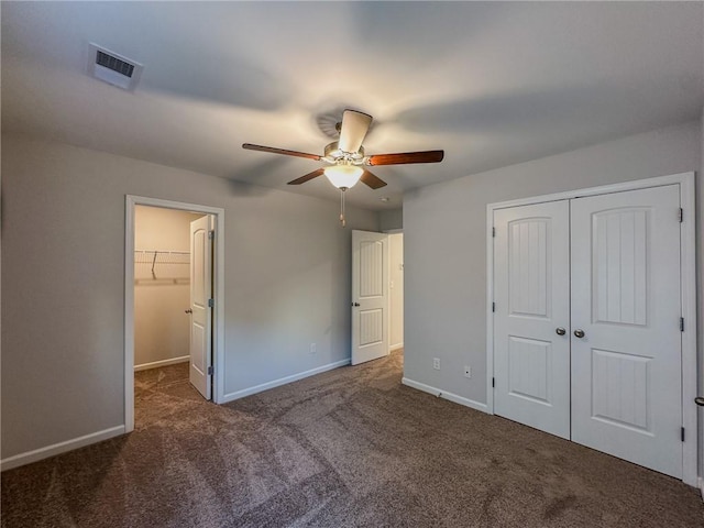 unfurnished bedroom with ceiling fan, a walk in closet, and dark colored carpet