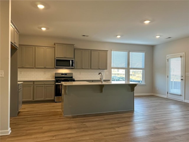 kitchen featuring stainless steel appliances, gray cabinets, a kitchen island with sink, light wood-type flooring, and a breakfast bar area