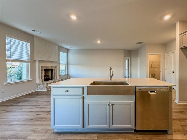 kitchen featuring a fireplace, dishwasher, sink, white cabinetry, and an island with sink