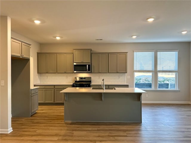 kitchen featuring an island with sink, appliances with stainless steel finishes, gray cabinetry, light wood-type flooring, and sink