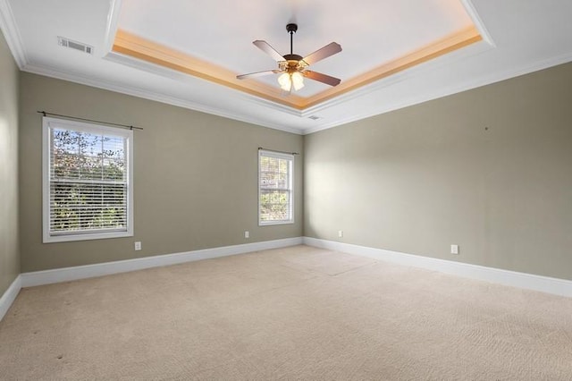 empty room with crown molding, ceiling fan, a tray ceiling, and light carpet