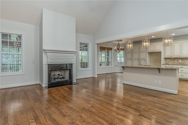 unfurnished living room with high vaulted ceiling, plenty of natural light, dark wood-type flooring, and sink