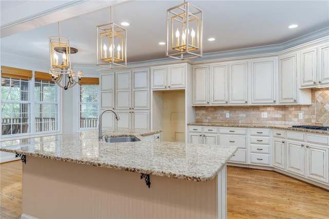 kitchen featuring decorative backsplash, ornamental molding, sink, decorative light fixtures, and a center island with sink