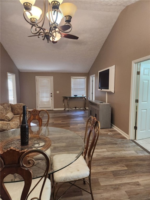 dining space with hardwood / wood-style floors, ceiling fan with notable chandelier, and lofted ceiling