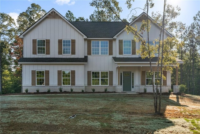view of front of home featuring board and batten siding, brick siding, roof with shingles, and a front lawn