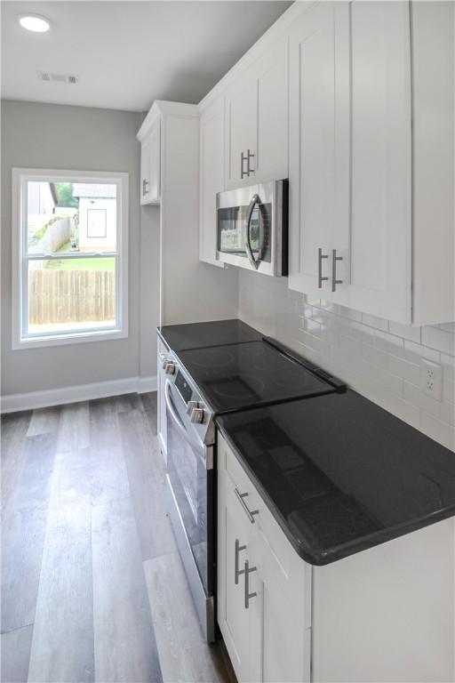 369 Lightness Dr, Auburn, AL 36832 - kitchen featuring appliances with stainless steel finishes, dark countertops, white cabinets, backsplash, and wood finished floors