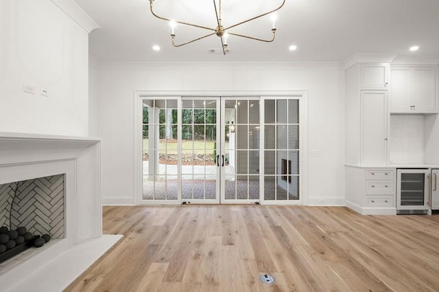 unfurnished living room with wine cooler, crown molding, a chandelier, and light hardwood / wood-style flooring