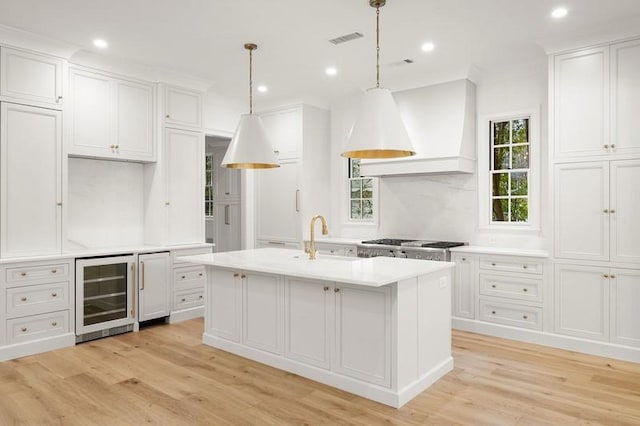 kitchen featuring decorative light fixtures, a center island with sink, custom range hood, wine cooler, and sink