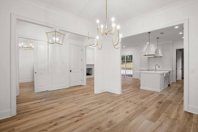 unfurnished dining area featuring sink, an inviting chandelier, ornamental molding, and light hardwood / wood-style flooring