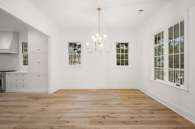 unfurnished dining area featuring light wood-type flooring, crown molding, and a chandelier