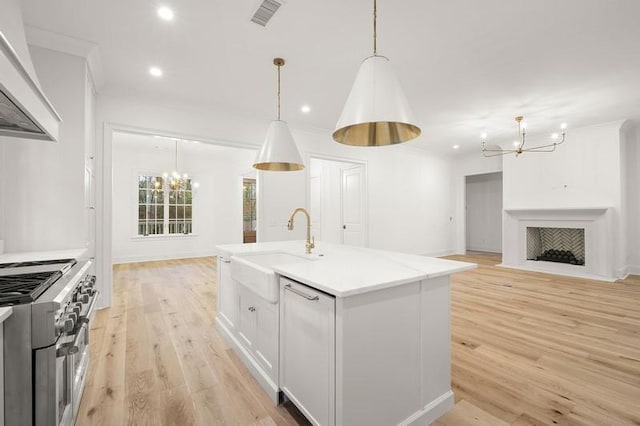 kitchen with hanging light fixtures, an island with sink, custom range hood, white cabinetry, and sink