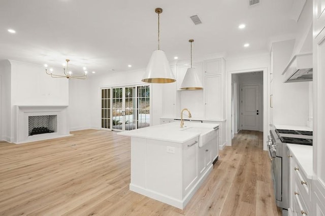 kitchen featuring stainless steel range, white cabinetry, pendant lighting, and an island with sink