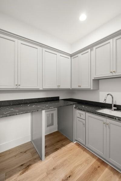 kitchen featuring sink, dark stone countertops, light wood-type flooring, and gray cabinets