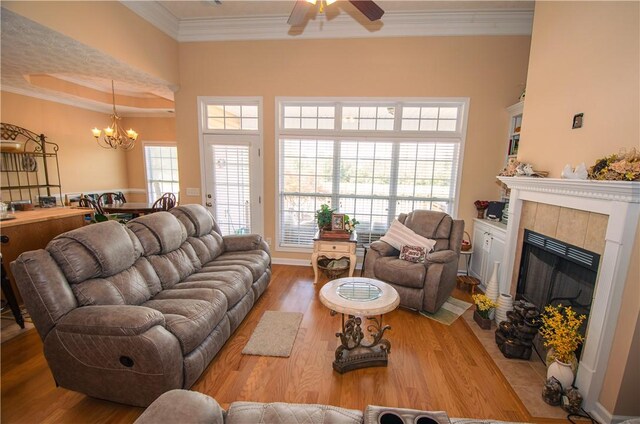 living room with hardwood / wood-style flooring, ceiling fan with notable chandelier, crown molding, and a tile fireplace