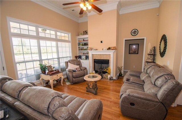 living room with light wood-type flooring, ceiling fan, crown molding, and a tiled fireplace