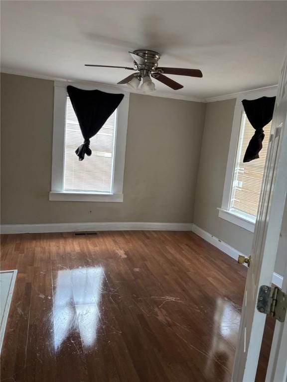 unfurnished room featuring crown molding, plenty of natural light, baseboards, and wood finished floors