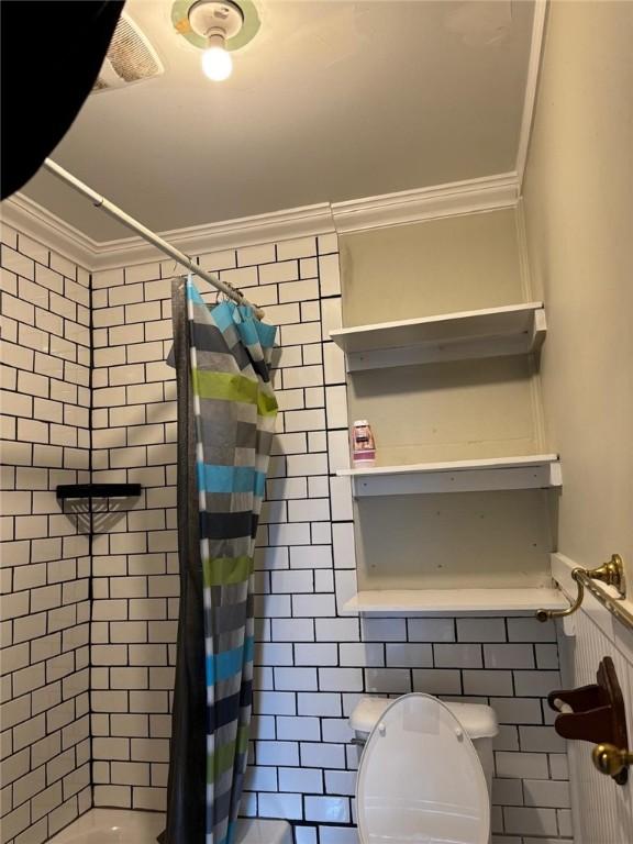 bathroom with visible vents, a shower with shower curtain, toilet, crown molding, and tile walls