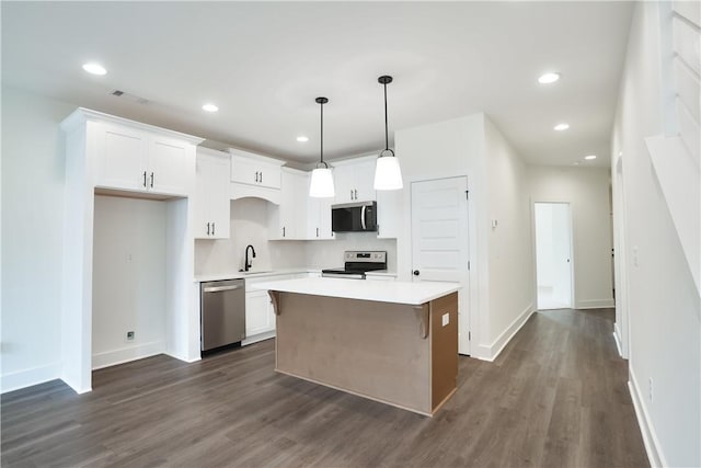 kitchen with dark wood-type flooring, stainless steel appliances, a kitchen island, pendant lighting, and white cabinets