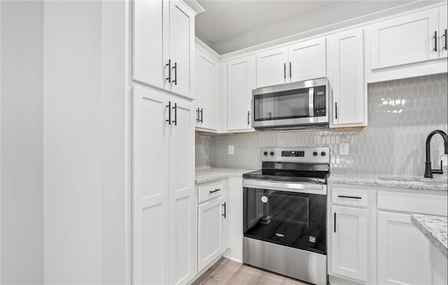 kitchen with appliances with stainless steel finishes, white cabinetry, a sink, and tasteful backsplash