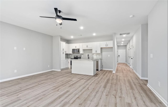 kitchen with light wood-style flooring, stainless steel appliances, a kitchen island, white cabinets, and light stone countertops