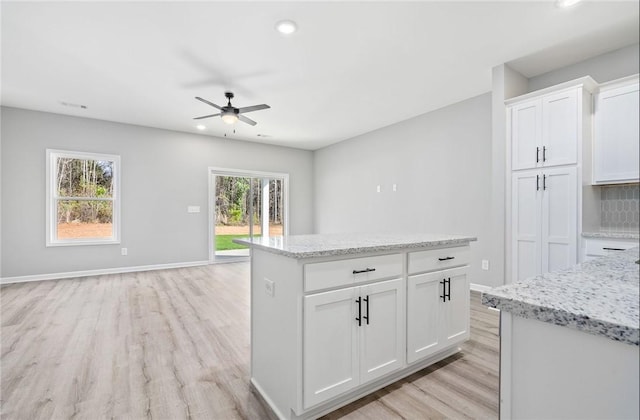 kitchen featuring a kitchen island, white cabinetry, light wood-style floors, open floor plan, and light stone countertops