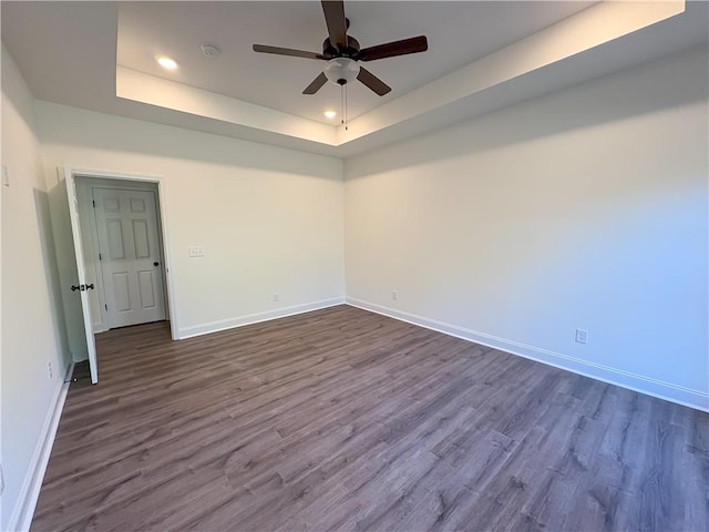 empty room with a raised ceiling, ceiling fan, and wood-type flooring