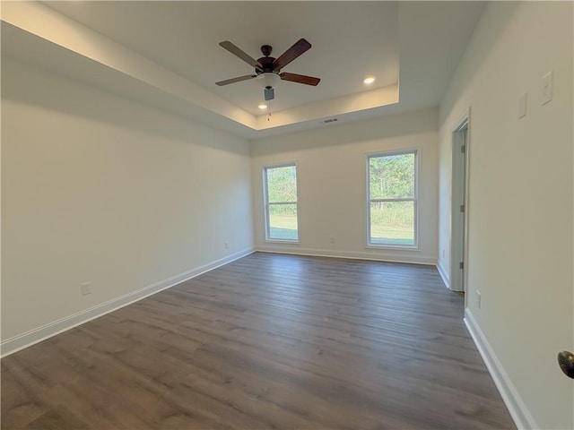 unfurnished room featuring ceiling fan, dark wood-type flooring, and a tray ceiling