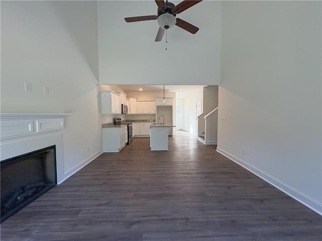 unfurnished living room featuring ceiling fan, dark hardwood / wood-style flooring, a towering ceiling, and sink