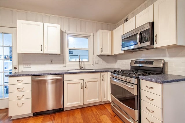 kitchen with sink, tasteful backsplash, appliances with stainless steel finishes, white cabinets, and light wood-type flooring