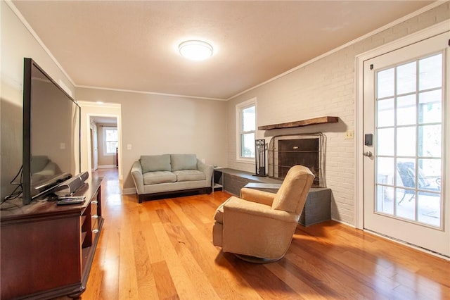 living room featuring light wood-type flooring, ornamental molding, brick wall, and a brick fireplace