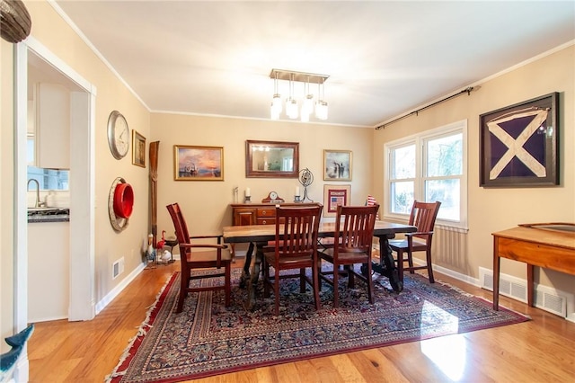 dining space featuring crown molding, light hardwood / wood-style flooring, a chandelier, and sink