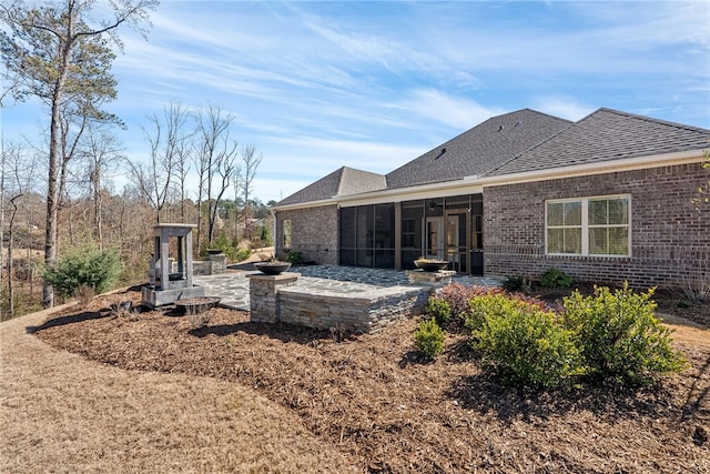 rear view of property featuring a patio, brick siding, roof with shingles, and a sunroom