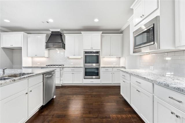 kitchen with custom range hood, white cabinetry, stainless steel appliances, and a sink