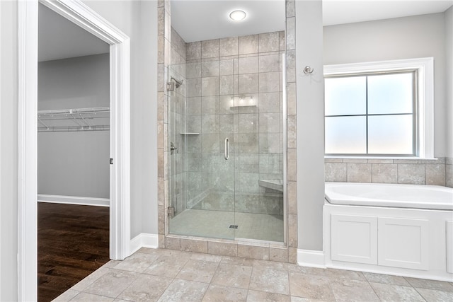 full bathroom with a stall shower, a walk in closet, a garden tub, and baseboards