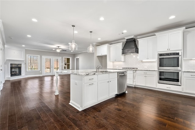 kitchen featuring stainless steel appliances, custom range hood, backsplash, open floor plan, and a sink