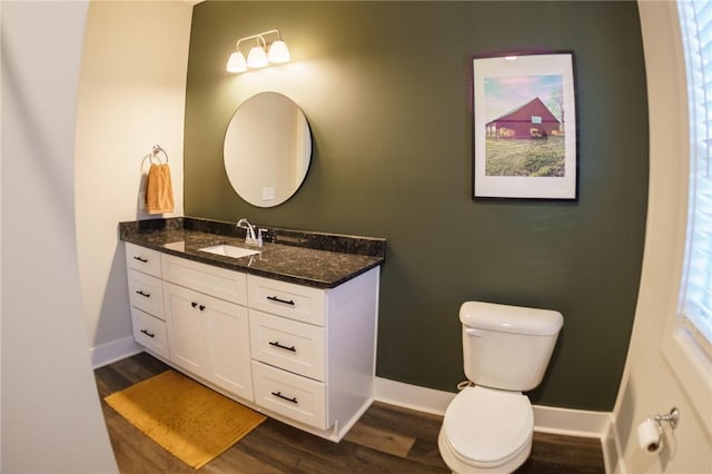 bathroom with toilet, vanity, baseboards, and wood finished floors