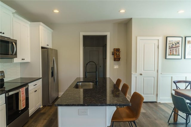 kitchen featuring a breakfast bar, an island with sink, a sink, white cabinets, and appliances with stainless steel finishes