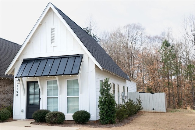 view of side of home with fence, a standing seam roof, a shingled roof, board and batten siding, and metal roof