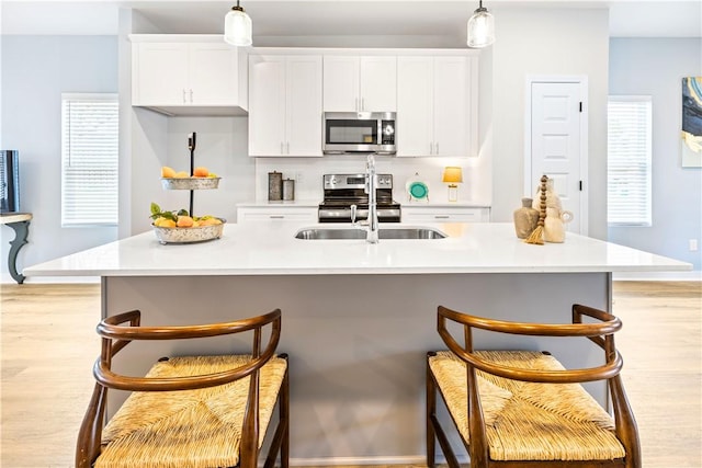 kitchen featuring a breakfast bar, stainless steel appliances, a kitchen island with sink, white cabinetry, and hanging light fixtures